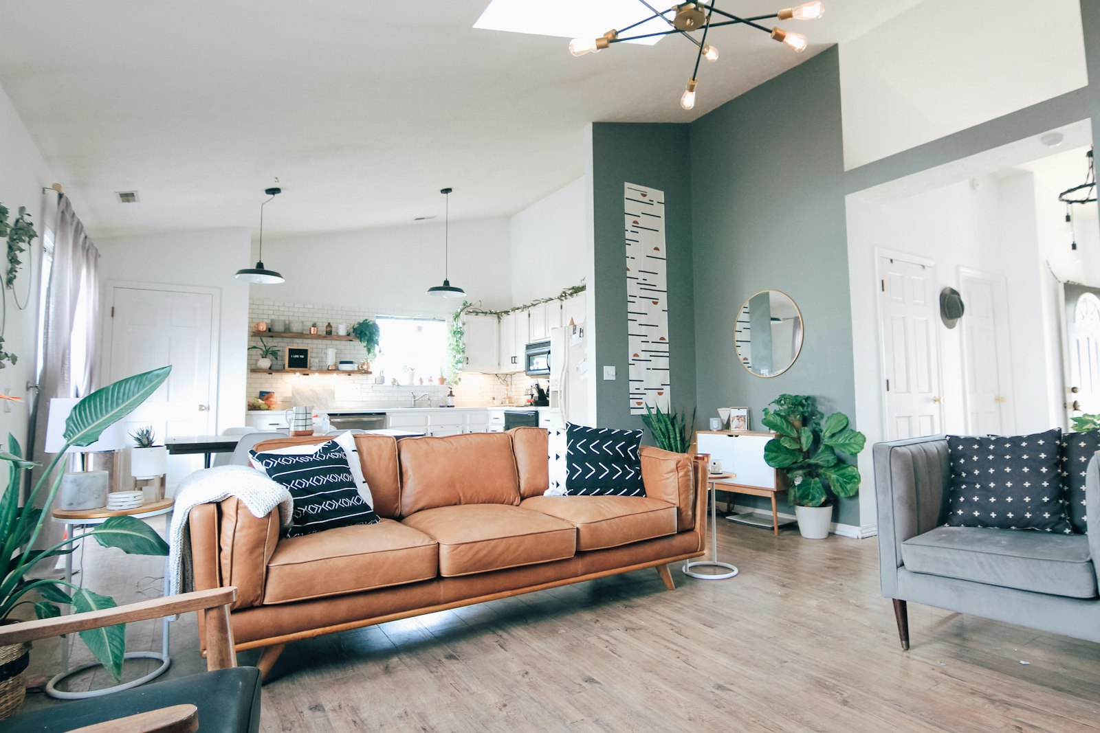 Open-plan living room with a leather sofa, houseplants and a kitchen beyond